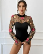 Front view of a model wearing a black embroidered rose lace bodysuit with sheer mesh long sleeves