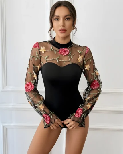 Front view of a model wearing a black embroidered rose lace bodysuit with sheer mesh long sleeves