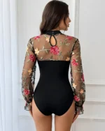 Back view of a black floral embroidered lace bodysuit with long sheer mesh sleeves