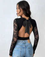 Back view of a black lace open back bodysuit paired with blue jeans and a bow tie detail